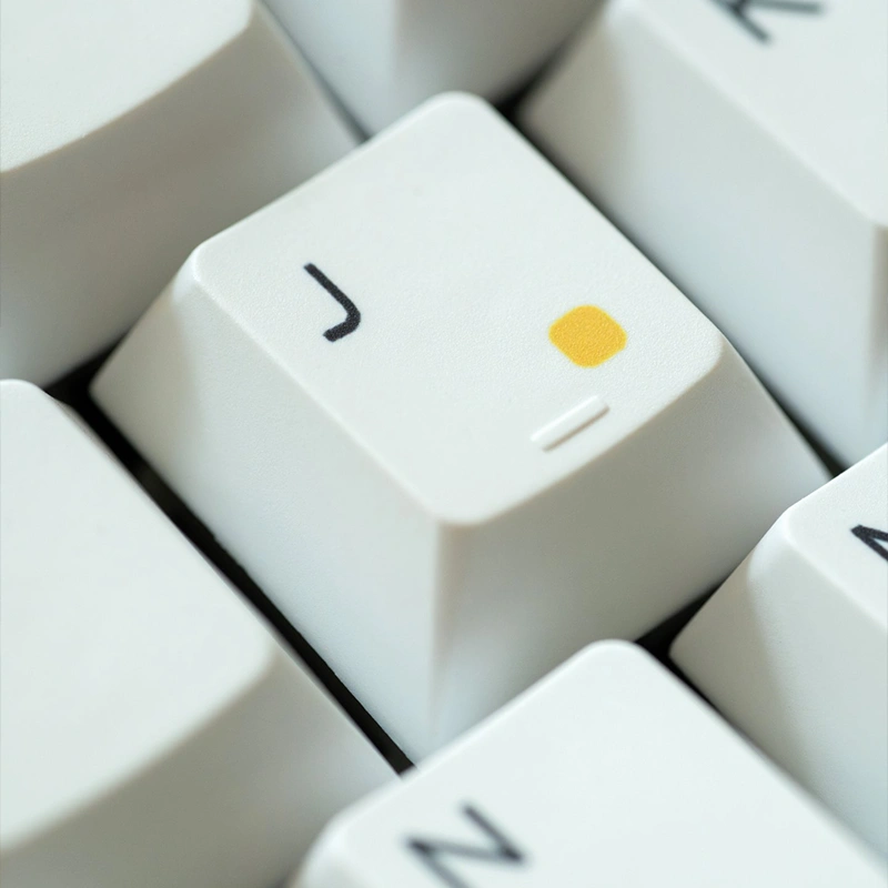 Close-up white keycap with yellow rainbow dot detail showing premium PBT construction