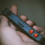 Hand holding black controller spacebar keycap showing matte finish texture, orange AB buttons, ergonomic design