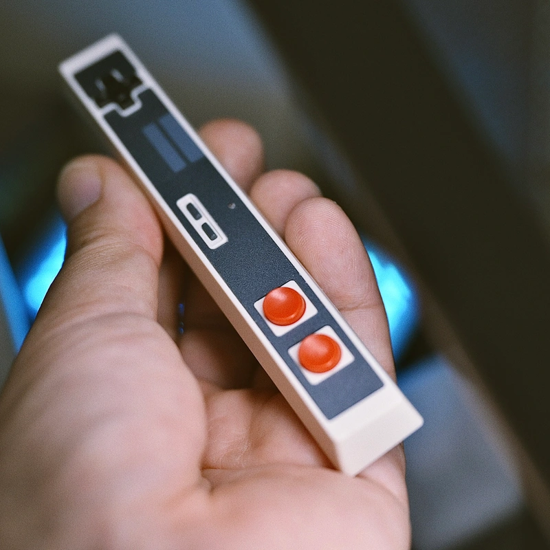 White-grey retro controller spacebar keycap in hand showing matte finish, orange buttons, enhanced tactile coating