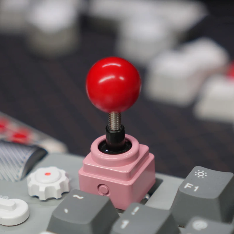 Pink Retro Joystick Artisan Keycap - Anodized Aluminum Gaming Accessory Pink anodized metal joystick keycap with red ball on keyboard, retro gaming artisan cap, customizable design