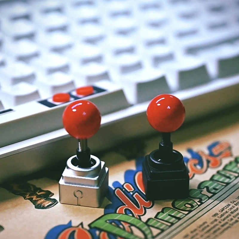Arcade Joystick Artisan Keycaps | Silver & Black Editions Two arcade joystick keycaps with red tops on colorful gaming artwork.