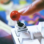 Hand moving red joystick keycap showing built-in servo mechanism on white keyboard, authentic arcade tactile feel
