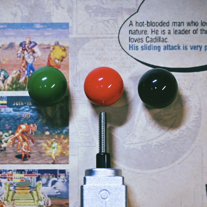 Retro Joystick Metal Artisan Keycap Three colored joystick balls (green, red, black) with metal base on retro gaming magazine background