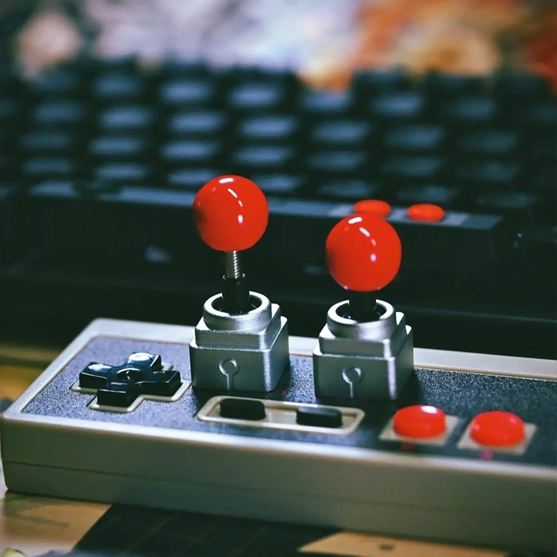 Retro Joystick Metal Artisan Keycap Two metal joystick keycaps on NES controller with red balls, retro gaming setup, arcade artisan caps display