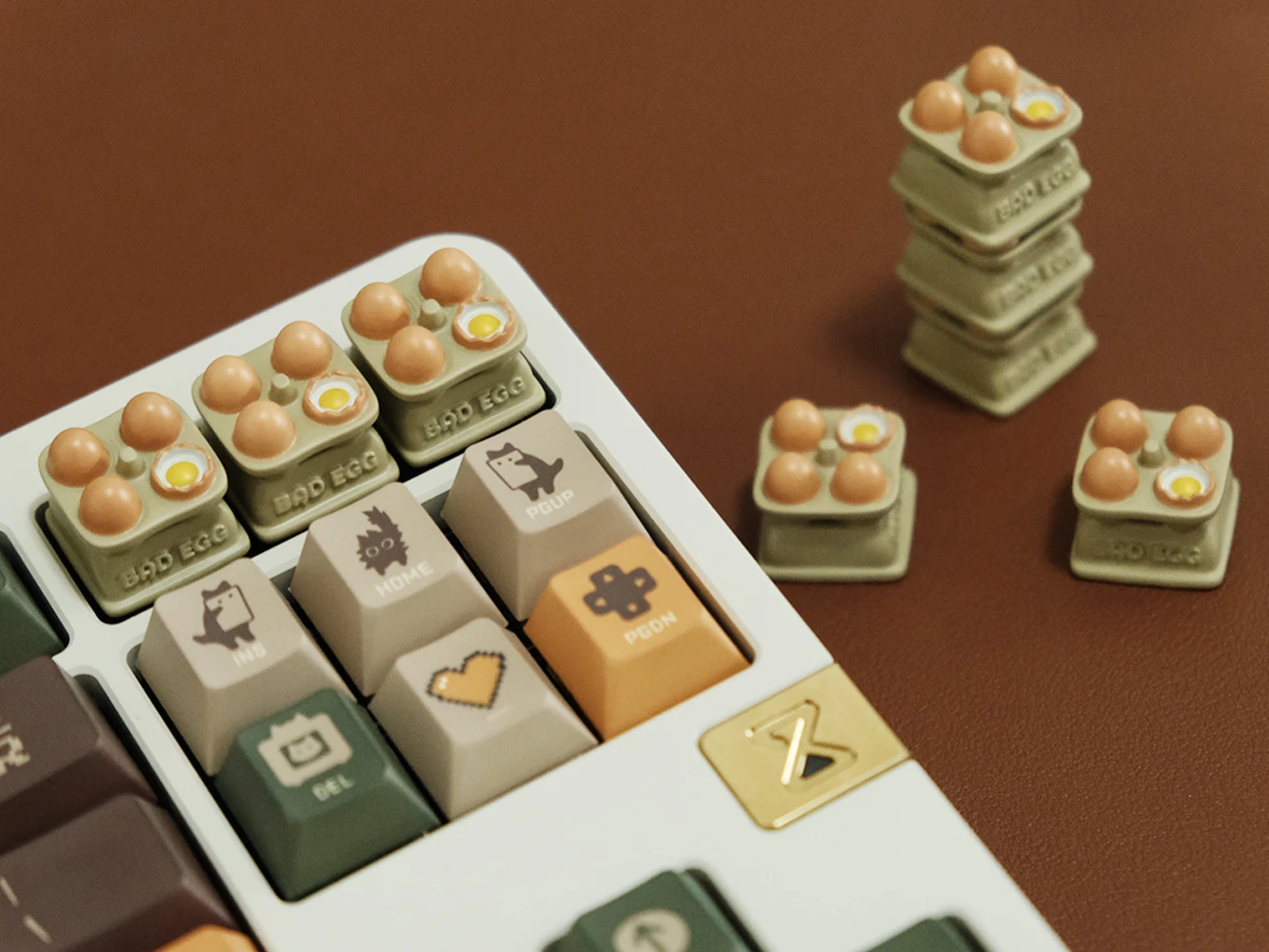 Multiple egg tray artisan keycaps installed on white keyboard numpad with hand-painted eggs, extra keycaps beside on brown desk