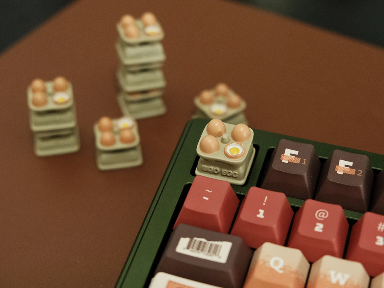 Egg tray artisan keycap mounted on green keyboard with stacked keycaps in background, featuring hand-painted eggs and yolk
