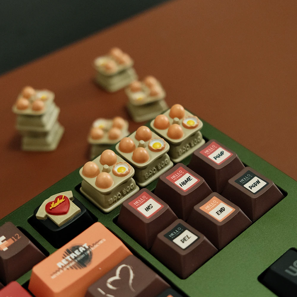 Egg tray artisan keycaps installed on green mechanical keyboard number row with hand-painted eggs, surrounded by extra keycaps