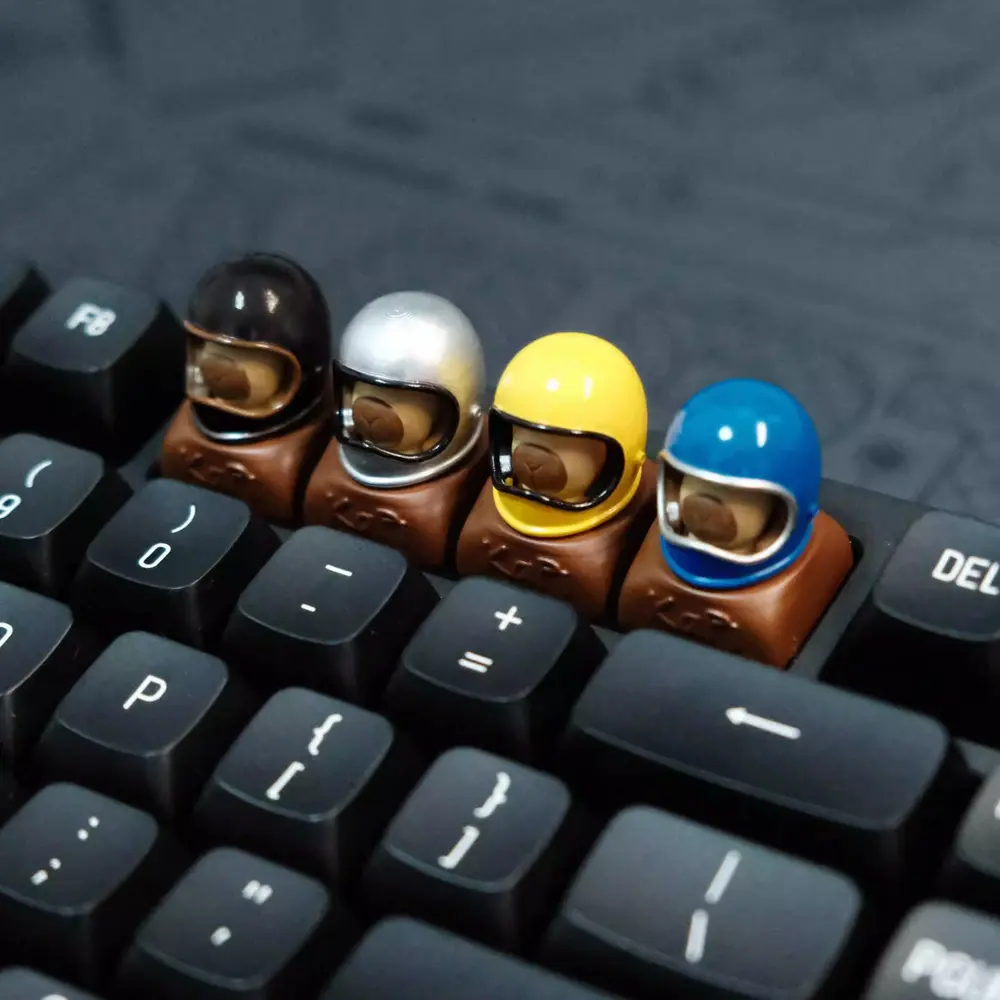 Four Helmeted Capybara Artisan Keycaps Set Row of cute capybara custom resin keycaps wearing colorful helmets on a black mechanical keyboard.