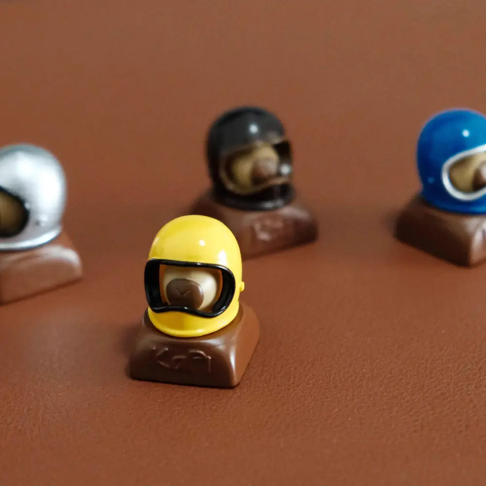 Yellow Helmeted Capybara Artisan Keycap Group Close-up of a yellow capybara custom resin keycap with other color variants on a brown surface.