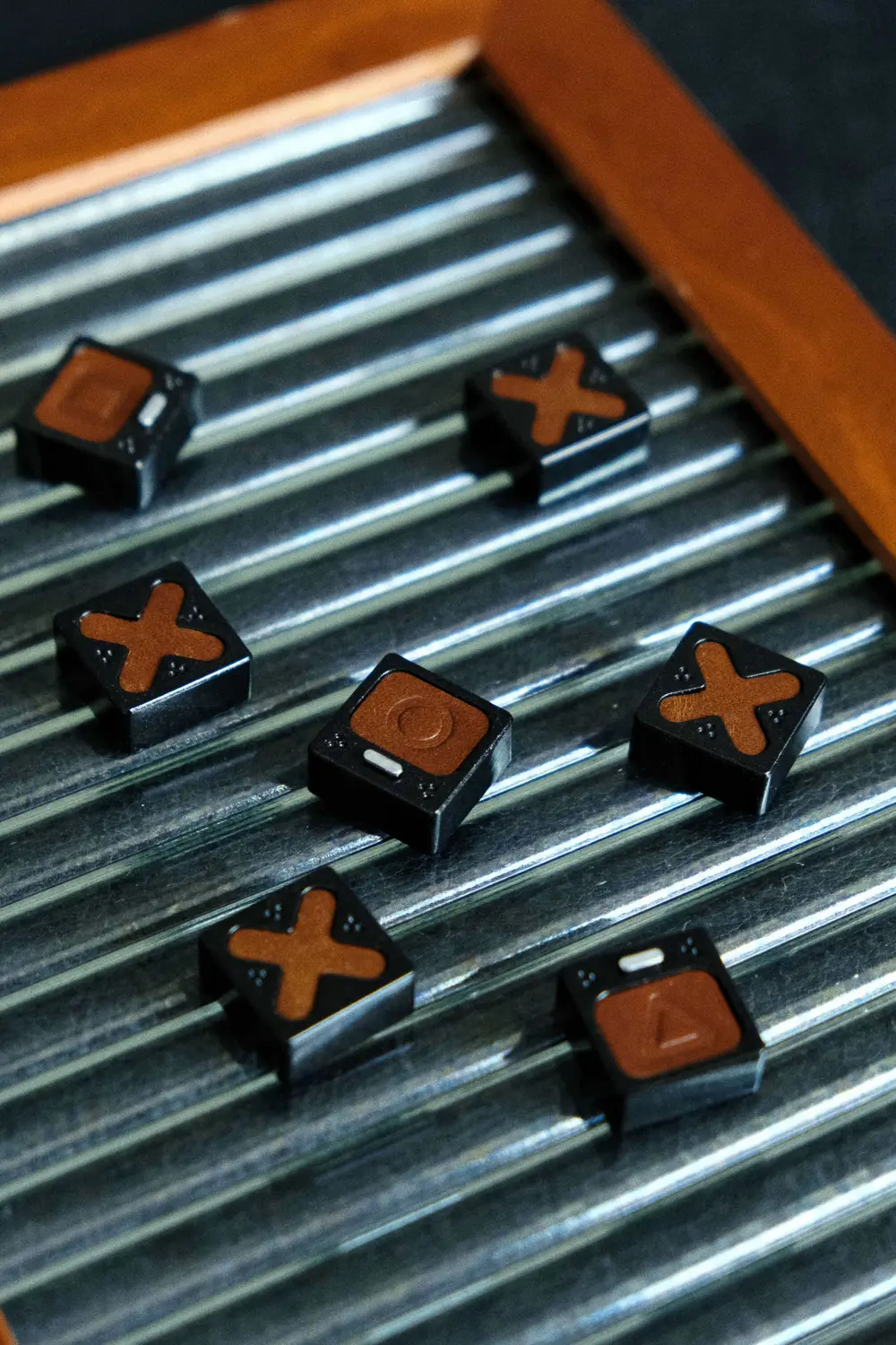 Genuine Leather PlayStation Symbols Artisan Keycaps Genuine leather PlayStation symbols artisan keycaps arranged on a silver grooved metal surface.