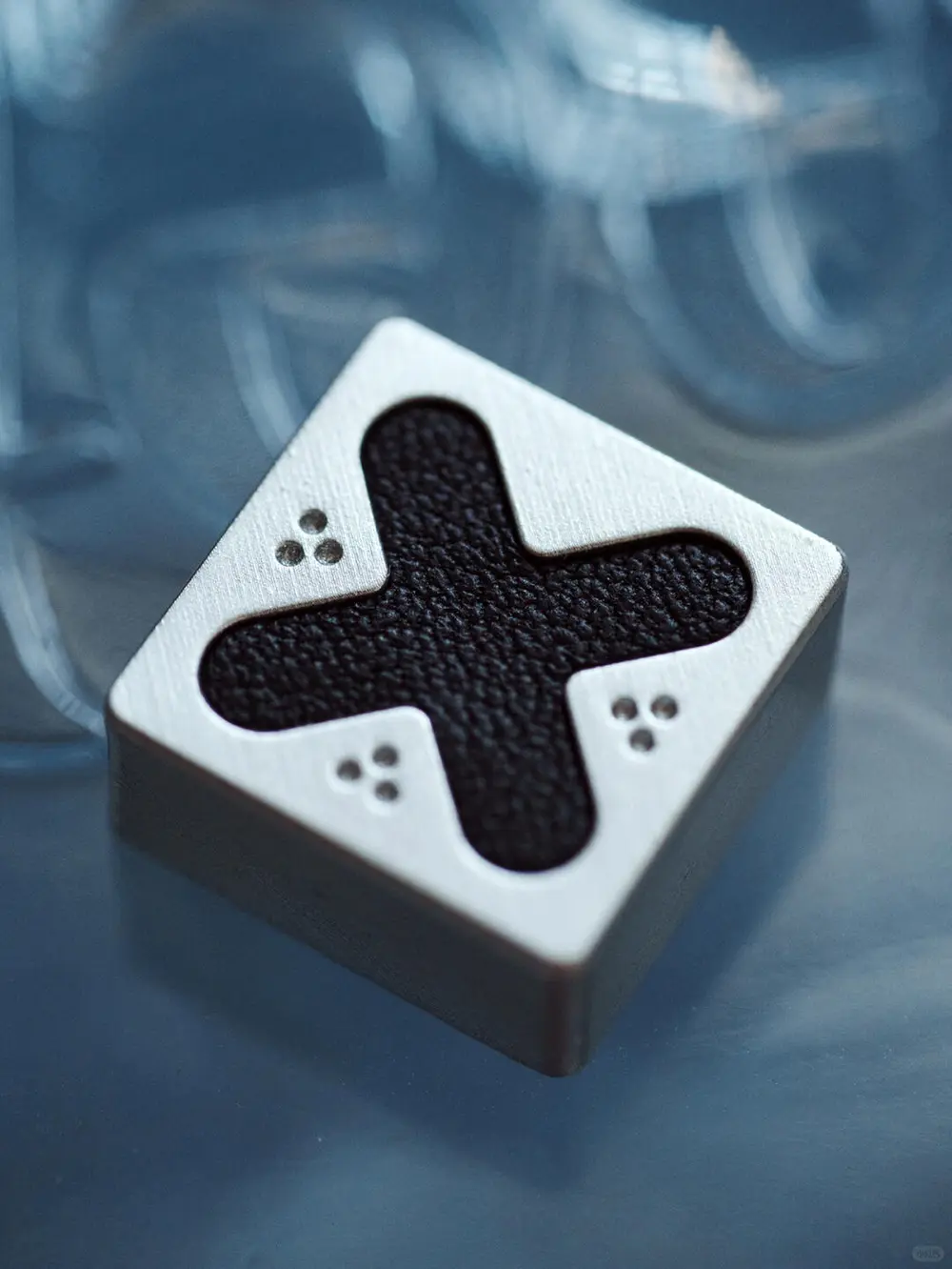 Silver Cross Leather Artisan Keycap Genuine leather PlayStation Cross keycap with metallic silver finish and textured grain.
