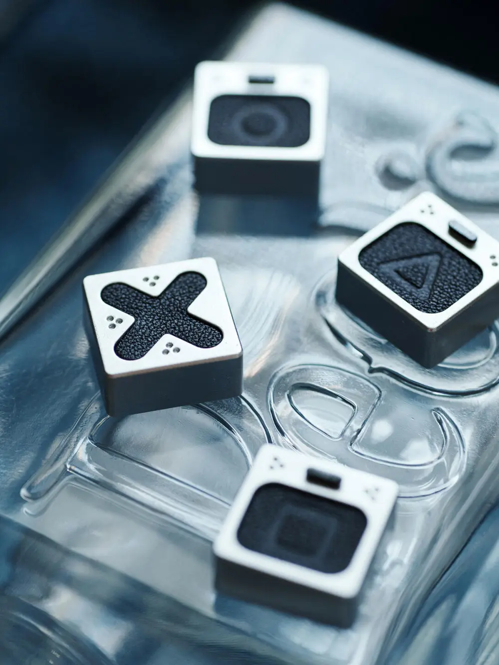 Genuine Leather PlayStation Symbols Artisan Keycaps Genuine leather playstation keycaps with metallic silver frames and textured black surfaces on glass.