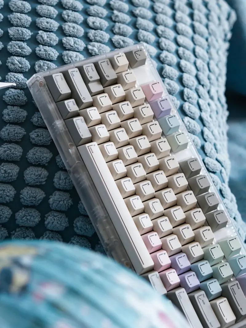 Angled view of Pastel Keycaps with minimalist line art legends on a clear keyboard case resting on blue fabric.