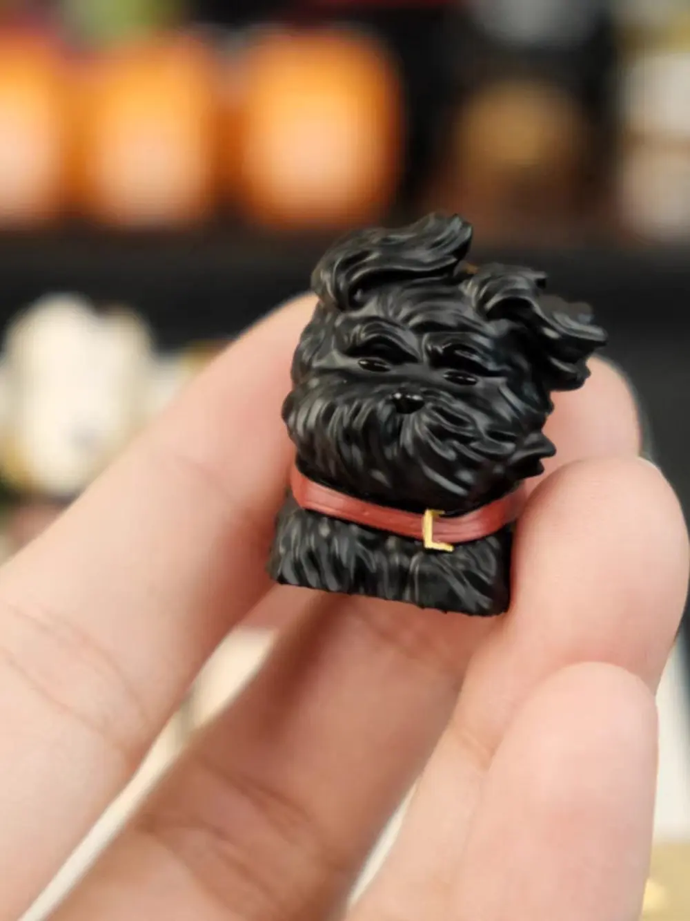 Black 3D printed resin puppy keycap with wind-swept fur and red collar held in hand.