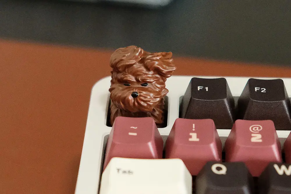 Coffee resin artisan keycap shaped like a wind-blown puppy on a keyboard corner.
