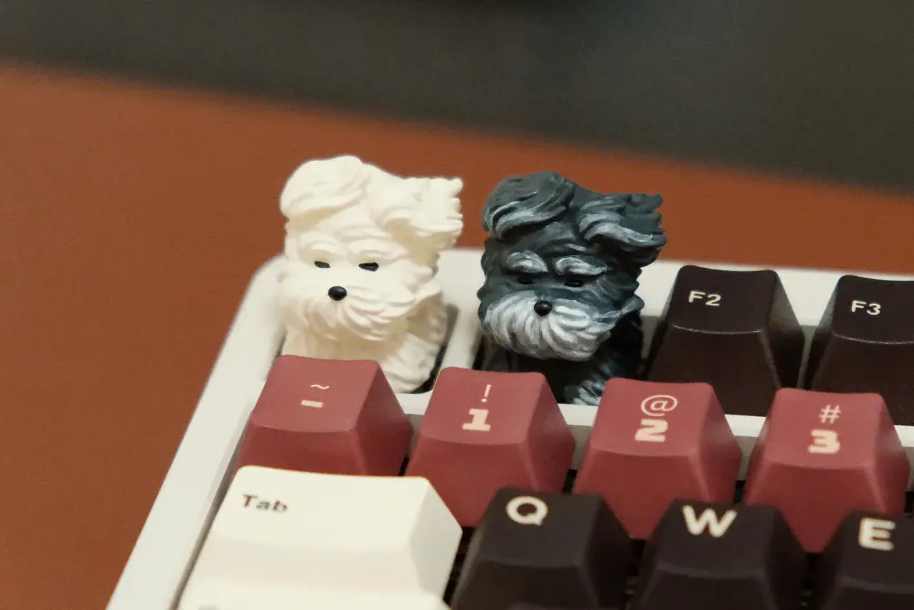 Side-by-side view of white and black 3D printed resin puppy keycaps with wind-swept details.