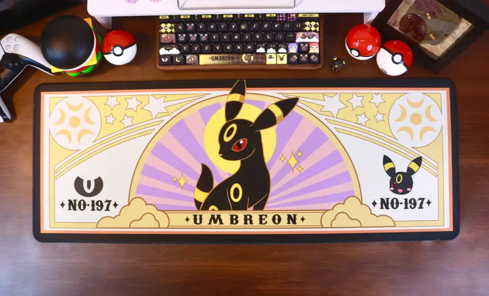 Pokemon Umbreon gaming desk mat centered on a desk with a custom keyboard, game controller, and Poke Balls.