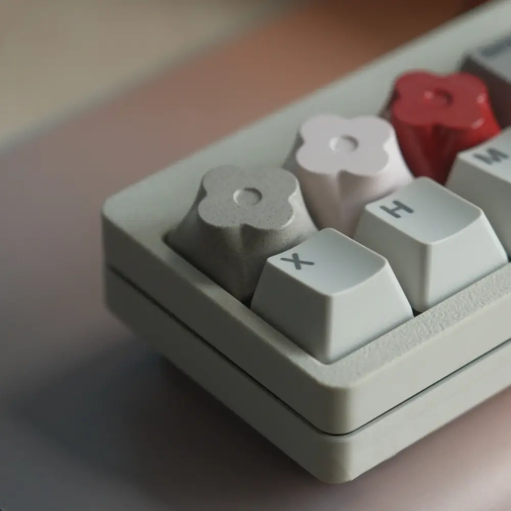 Close-up of three CNC aluminum floral artisan keycaps in gray, white, and red on a keyboard.