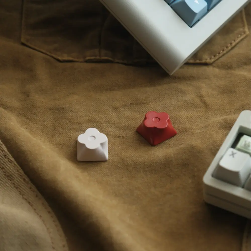 Blush White and Candy Red CNC aluminum flower metal keycaps displayed on a brown cloth surface.