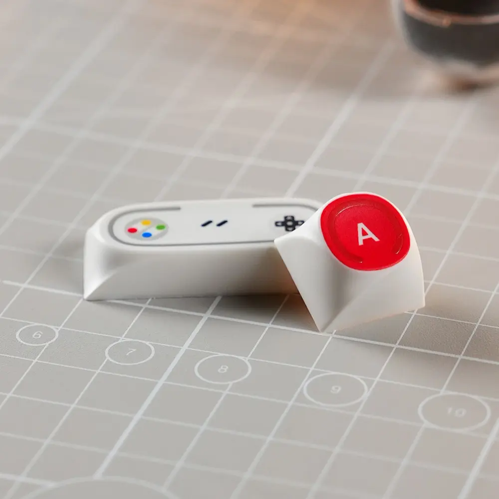 Game Console Theme Novelty Keycaps Close-up Two retro game console themed keycaps including a controller design and red A button.