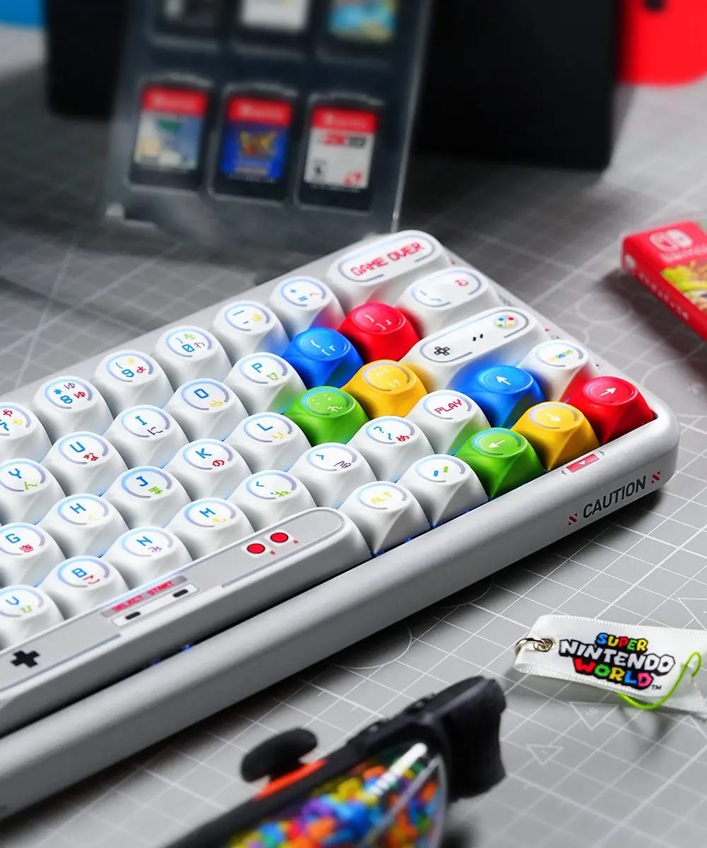 Game Console Theme Keycaps Angled Close Up Close-up of white MDA profile keycaps with retro game console legends and colorful translucent directional keys.