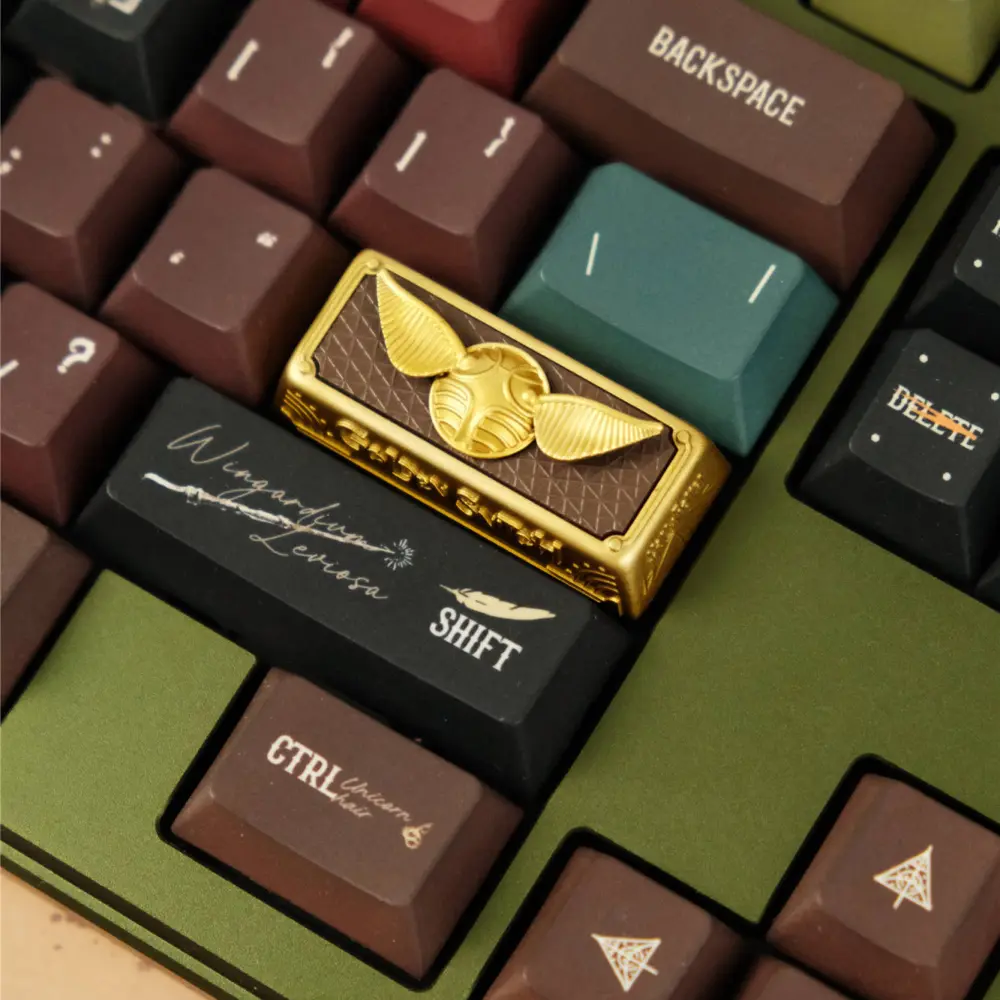 Gold-painted Harry Potter artisan keycap with a Snitch design mounted on a mechanical keyboard.