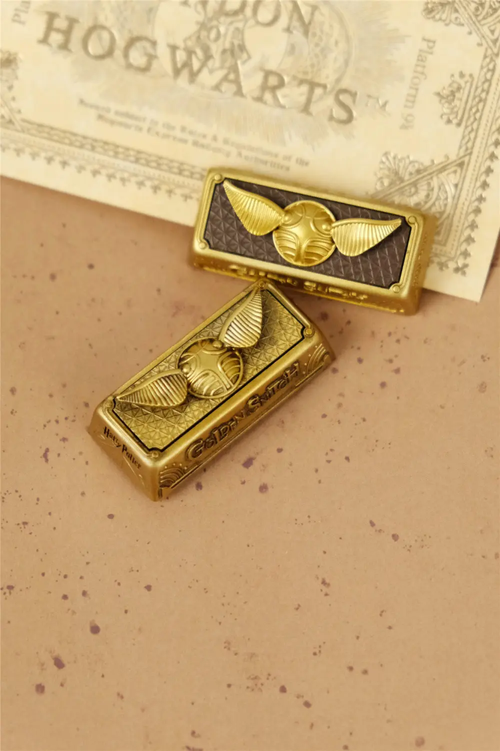 Two 2.25U artisan keycaps featuring the Golden Snitch design on a textured surface.