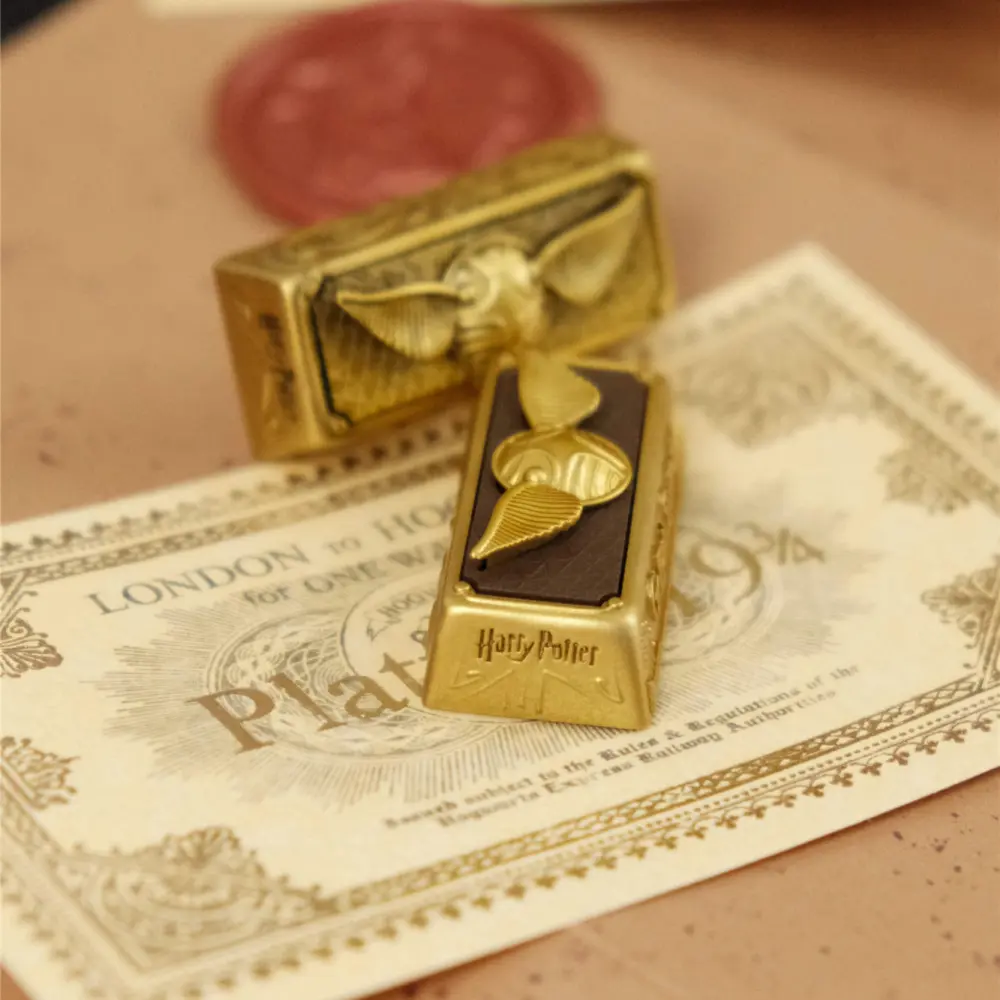 Vintage oxidized gold Golden Snitch artisan enter keycap resting on a Platform 9 3/4 train ticket.