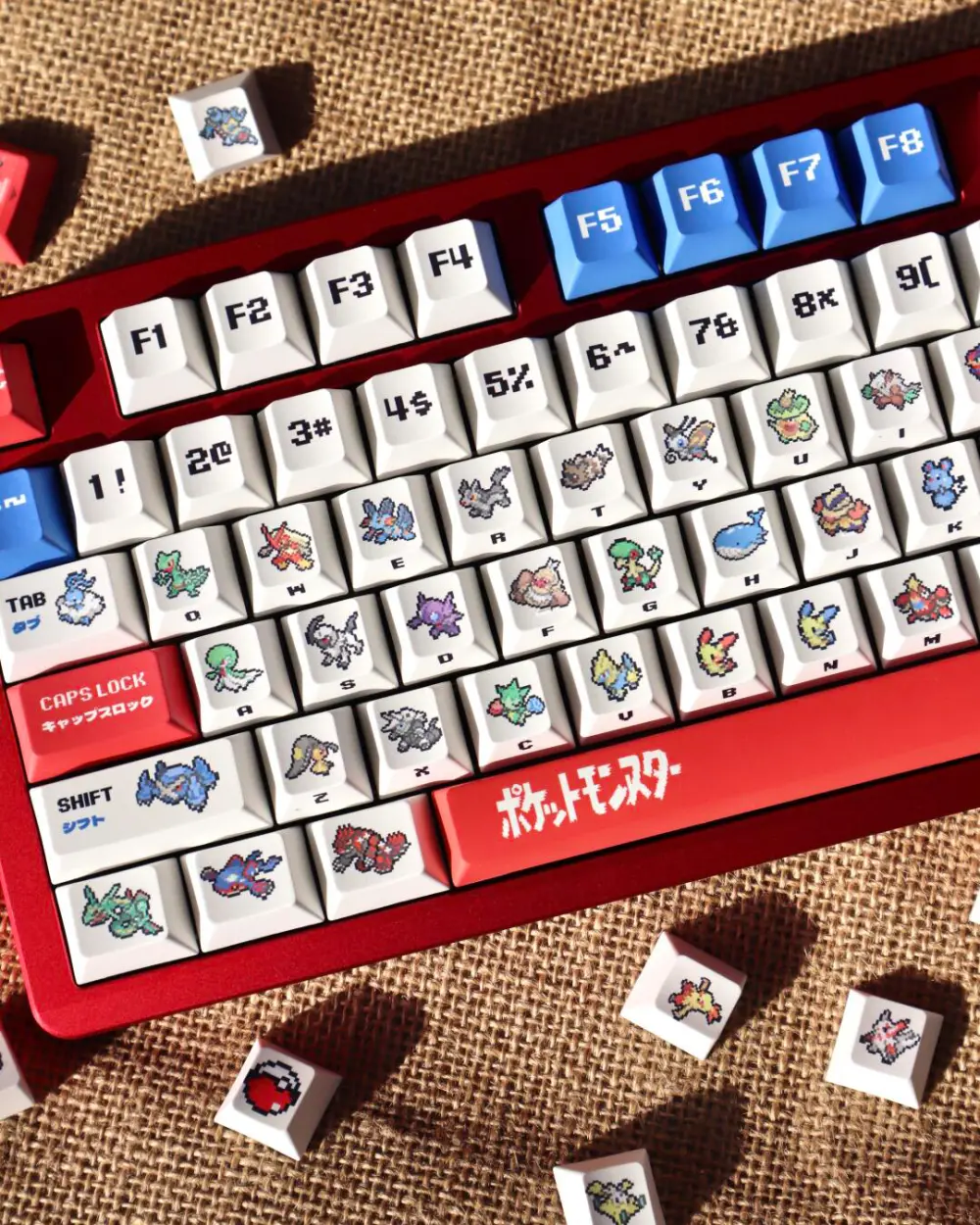 Top-down view of pixel art Pokemon keycaps on a red keyboard case including Groudon and Kyogre designs.