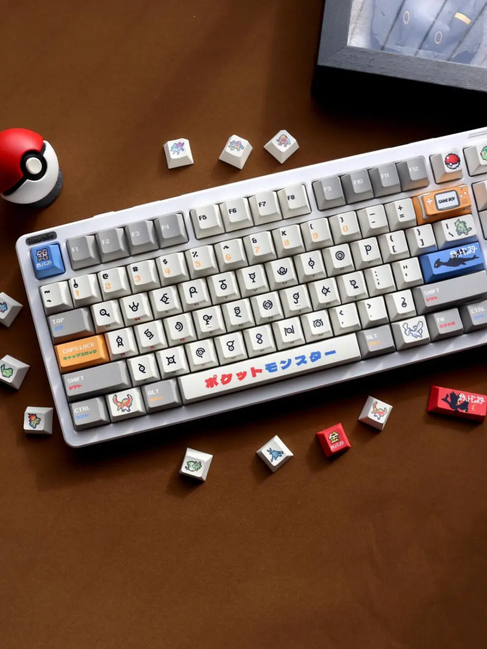 Pokemon Gold and Silver Unown keycaps on a white keyboard with pixel art novelty keys on a brown desk mat.