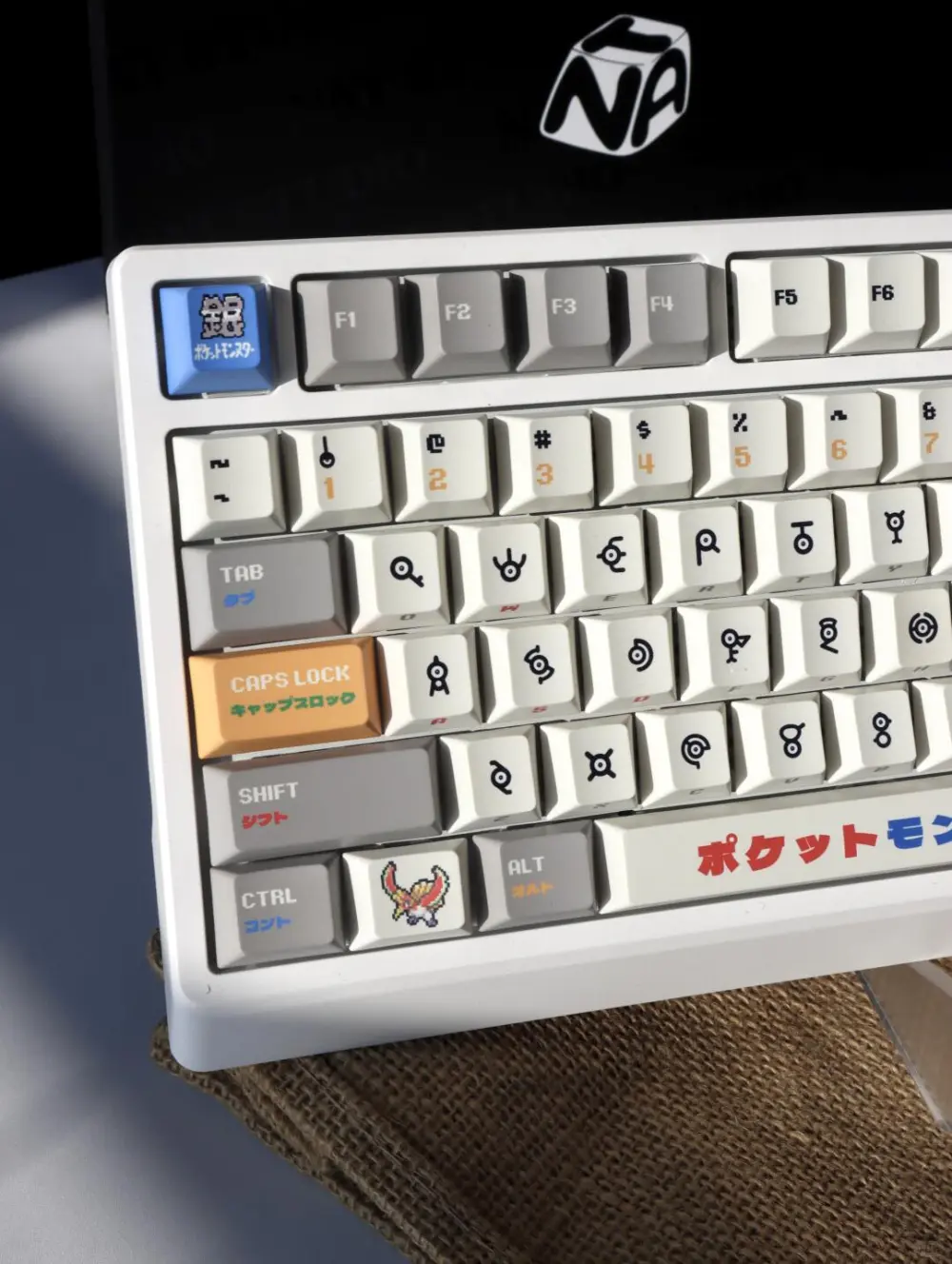 Pokemon Gold and Silver Unown Keycaps Left Side Left side view of a keyboard featuring Pokemon Unown keycaps, orange Caps Lock, and Ho-Oh novelty key.