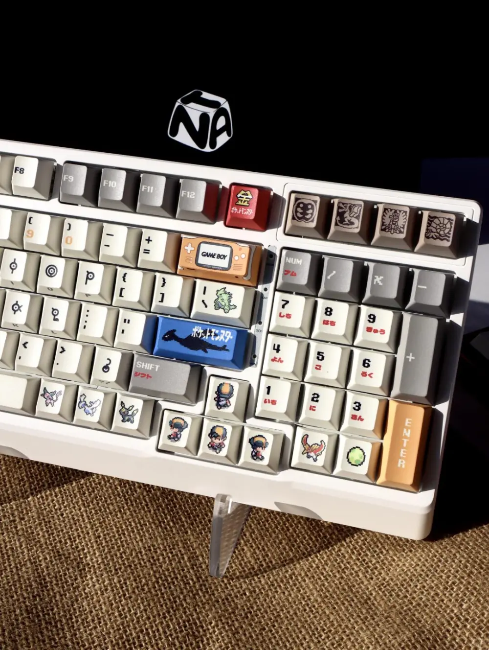 Pokemon Gold and Silver Unown Keycaps on Keyboard Close-up of Pokemon Unown keycaps on a white keyboard, showcasing retro pixel art designs and a blue Lugia novelty key.