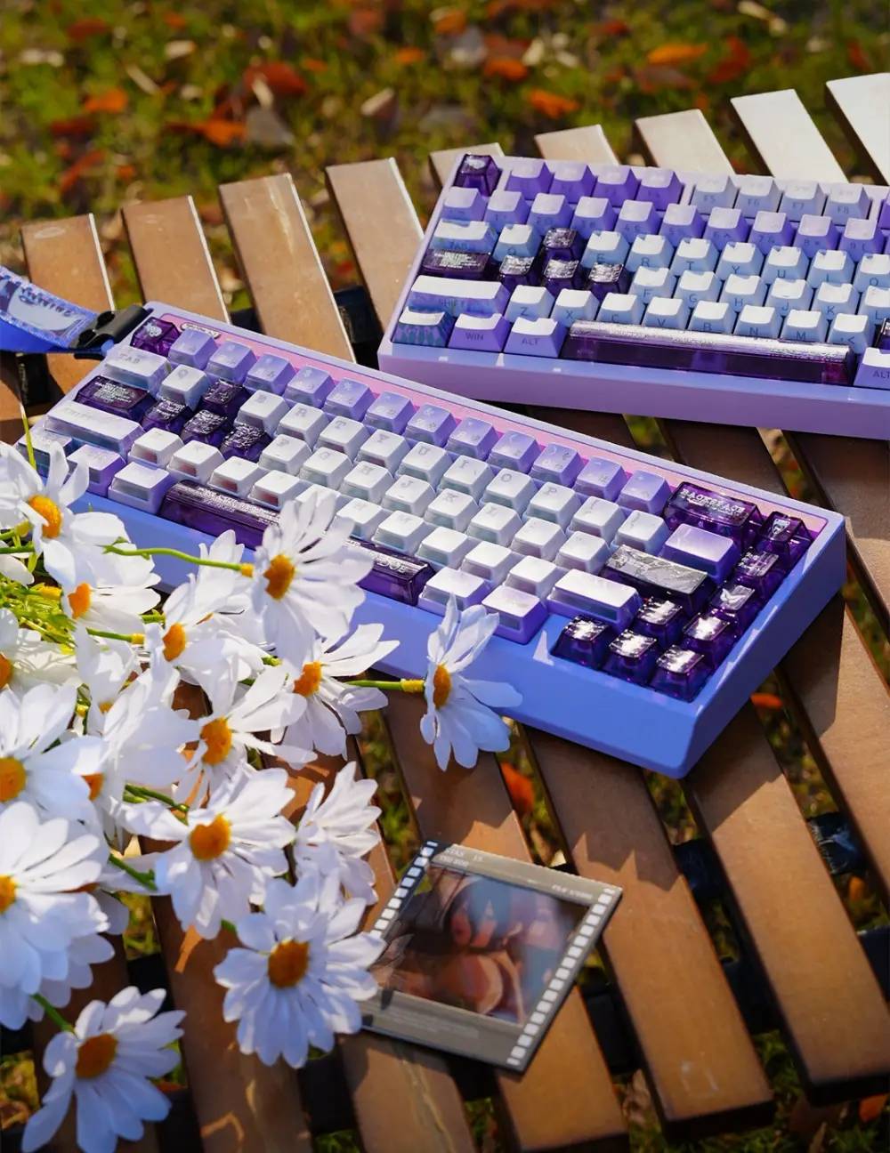 Chainsaw Man Reze Keycaps on Keyboards Outdoors Purple and white Reze keycaps on keyboards on a wooden table with daisy flowers and a Reze photo.