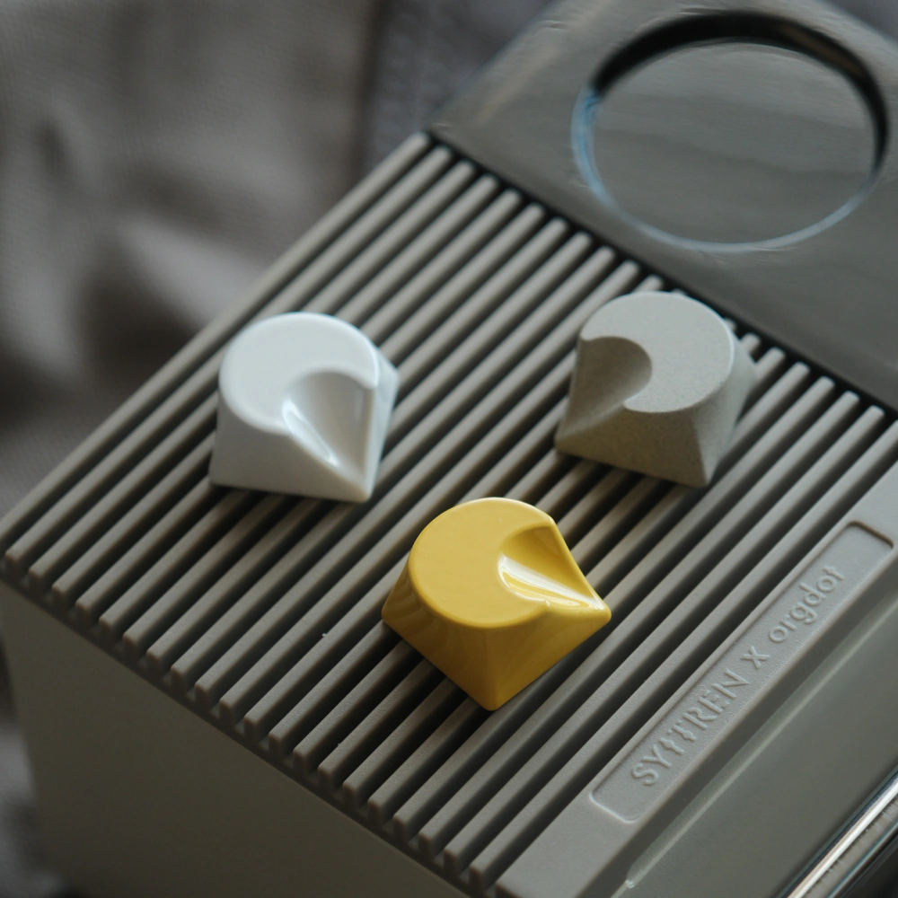 White, grey and yellow crescent-shaped aluminum keycaps placed on the surface of the grille.