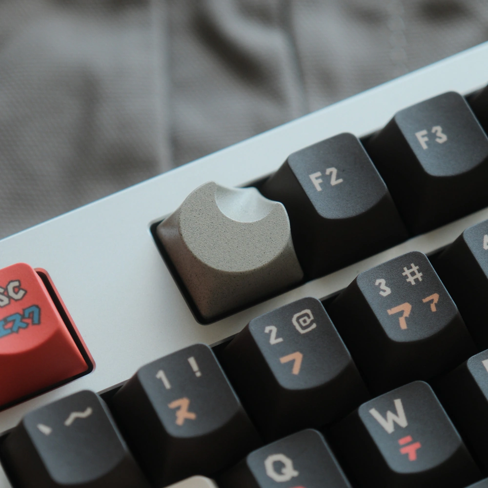 Grey CNC-machined aluminum keycap in a crescent moon shape installed on a white mechanical keyboard.