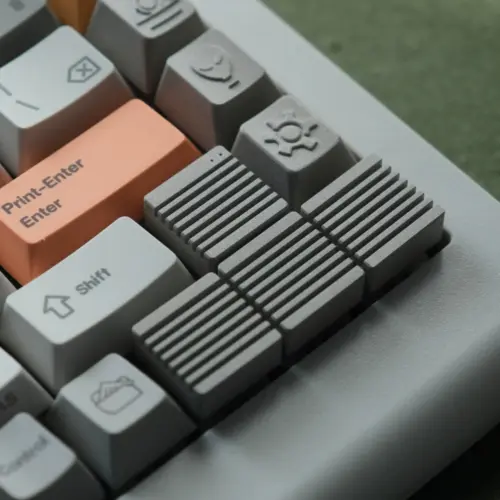 Linen Grey Heatsink Arrow Keys Metal Artisan Keycaps Four linen grey ribbed metal artisan keycaps replacing arrow keys next to an orange enter key on a keyboard.