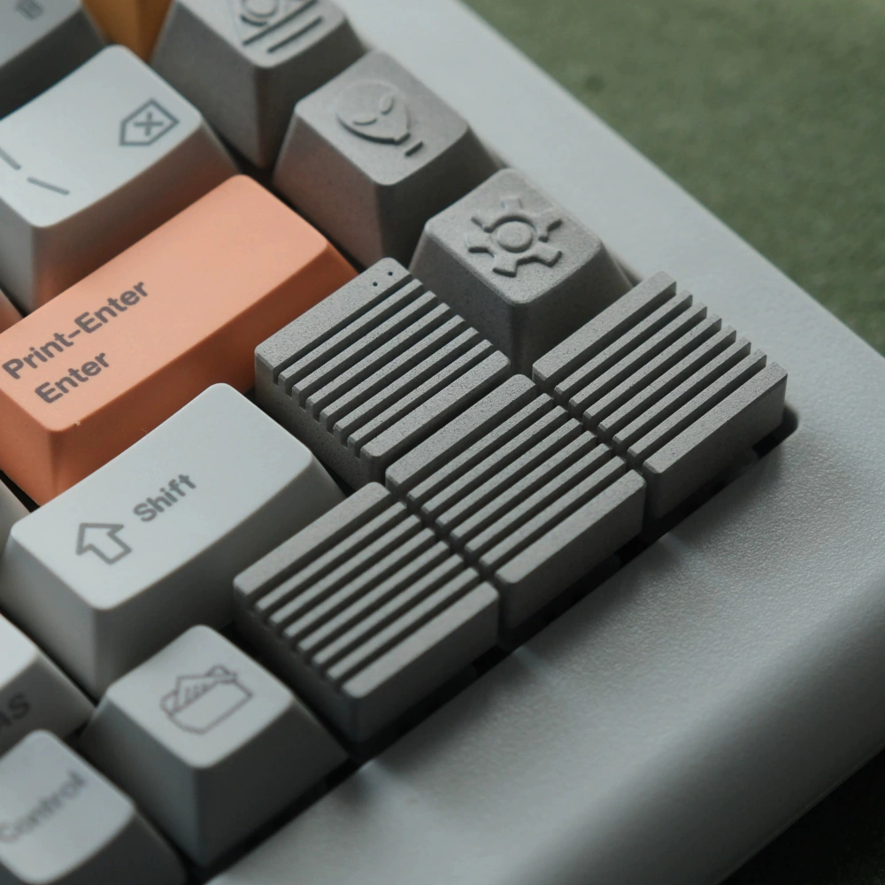 Linen Grey Heatsink Arrow Keys Metal Artisan Keycaps Four linen grey ribbed metal artisan keycaps replacing arrow keys next to an orange enter key on a keyboard.