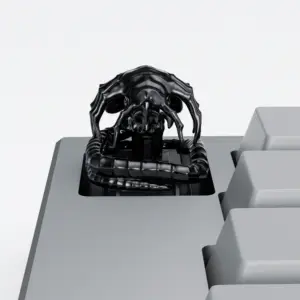 Black electroplated Alien Facehugger artisan keycap with ribbed tail on a grey keyboard.