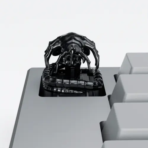 Black Alien Facehugger Artisan Keycap Black electroplated Alien Facehugger artisan keycap with ribbed tail on a grey keyboard.