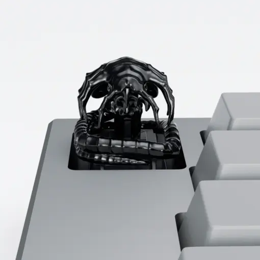 Black Alien Facehugger Artisan Keycap Black electroplated Alien Facehugger artisan keycap with ribbed tail on a grey keyboard.