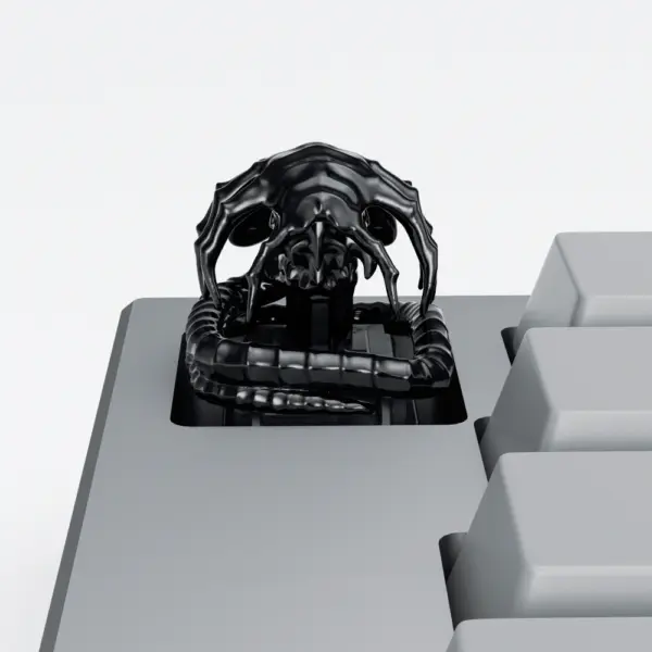 Black Alien Facehugger Artisan Keycap Black electroplated Alien Facehugger artisan keycap with ribbed tail on a grey keyboard.