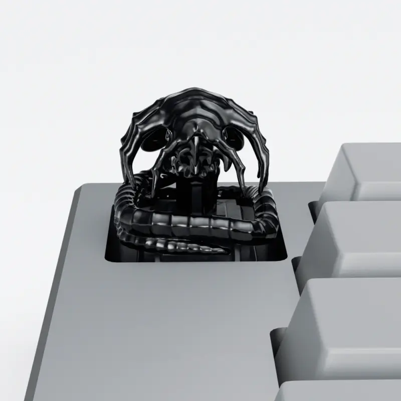 Black Alien Facehugger Artisan Keycap Black electroplated Alien Facehugger artisan keycap with ribbed tail on a grey keyboard.