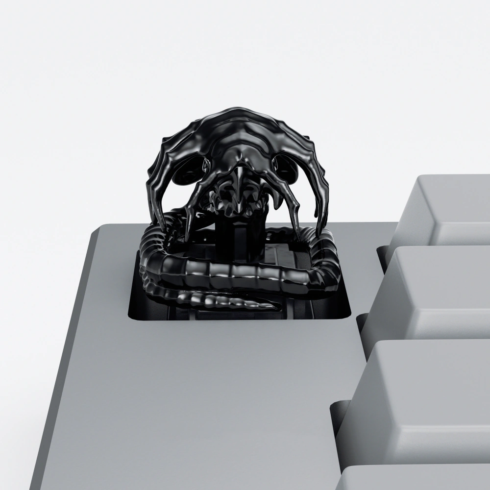 Black Alien Facehugger Artisan Keycap Black electroplated Alien Facehugger artisan keycap with ribbed tail on a grey keyboard.