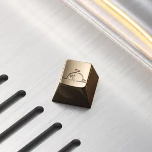 Cute Whale Brass Keycap Close Up Cute whale mirror polished brass artisan keycap resting on a slotted brushed metal background.
