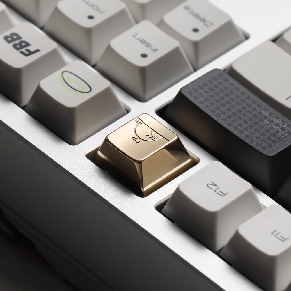 Gold-colored solid brass artisan keycap with a whale engraving placed among standard white and black keycaps.