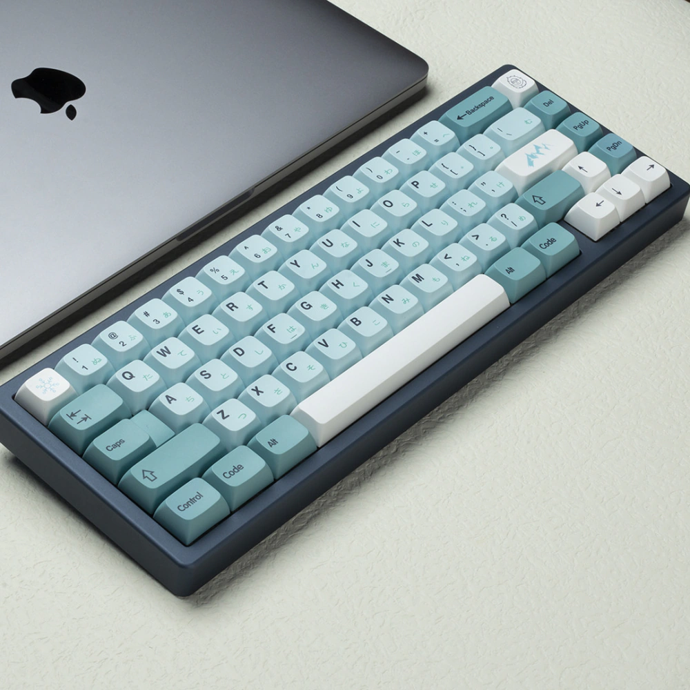 Compact keyboard with blue Japanese legend keycaps next to a silver laptop