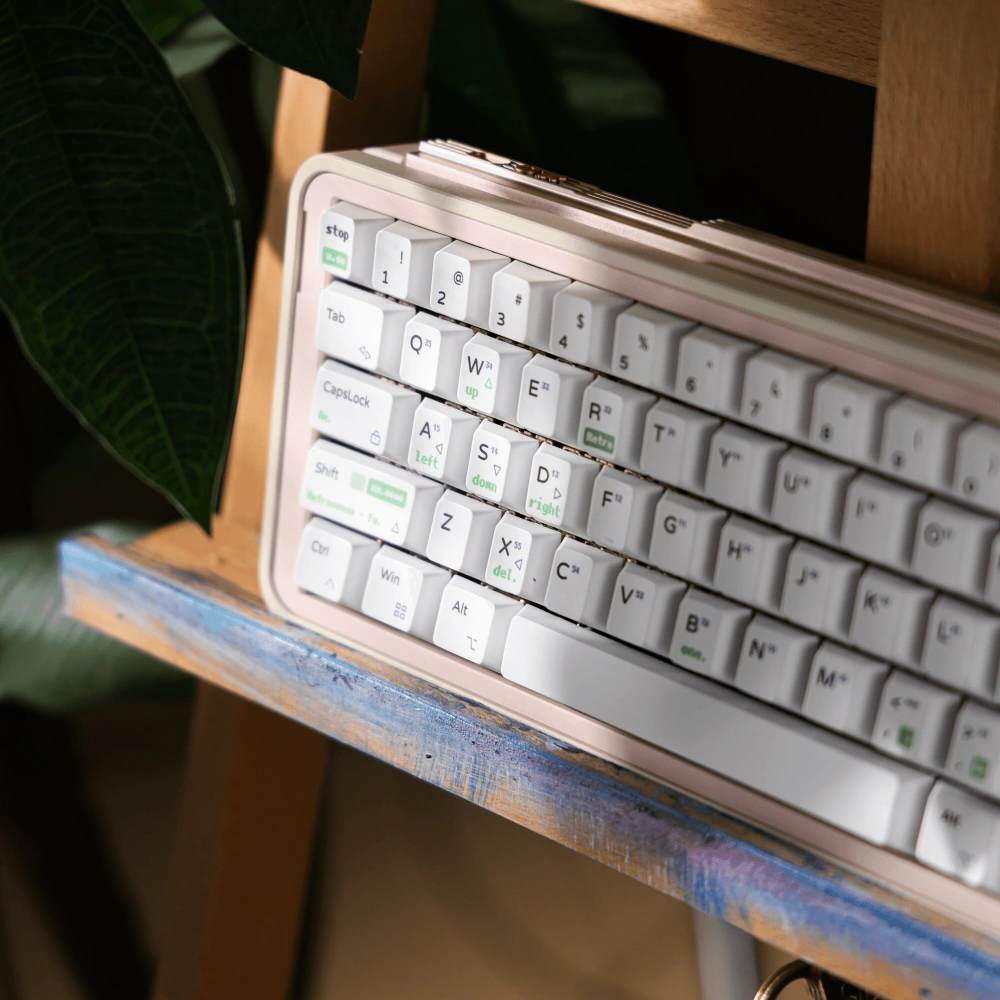White Cherry profile keycaps with neon green sub-legends on a rose gold keyboard next to a plant leaf.