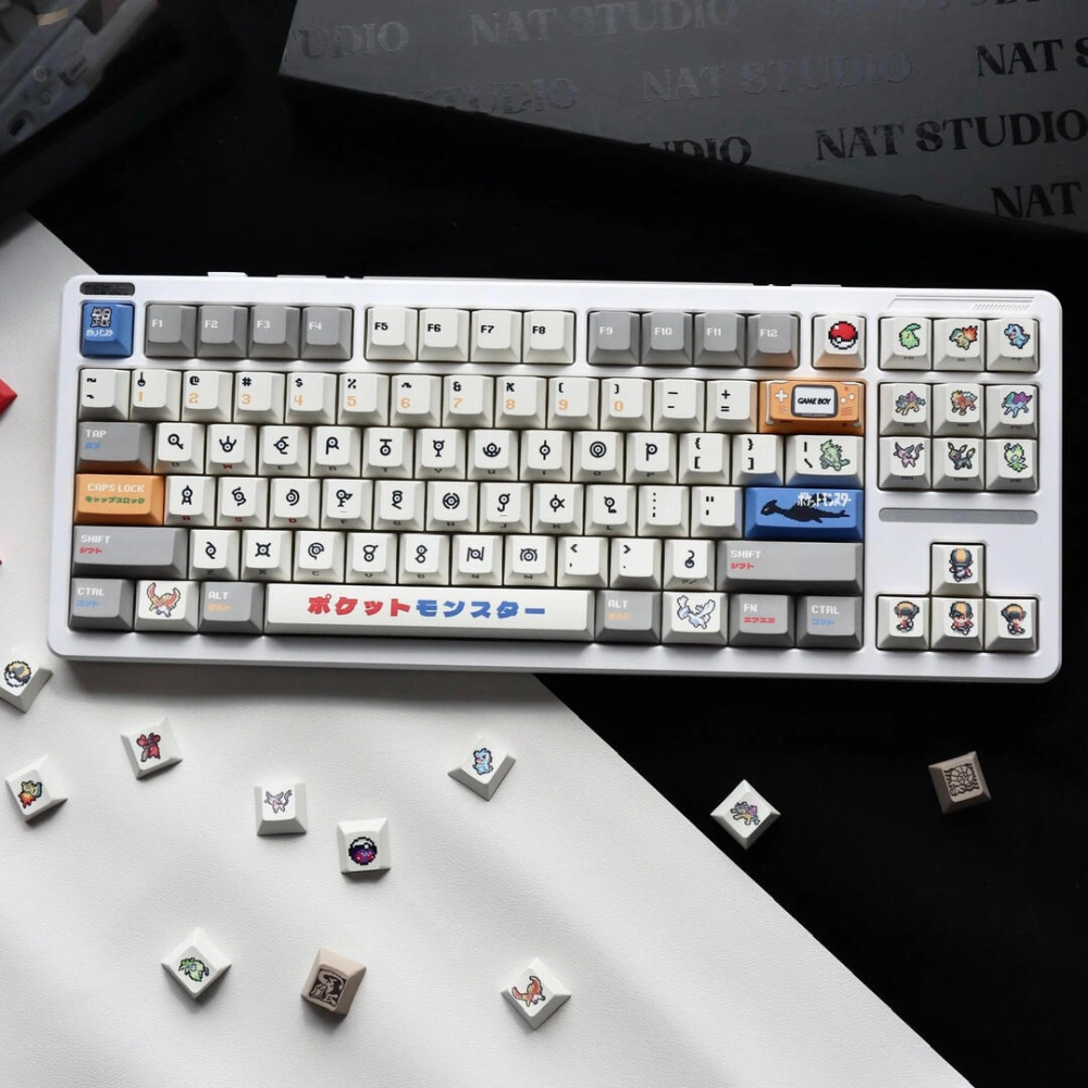 Overhead view of retro gold silver pixel keycaps on a keyboard with loose accent keys scattered on white desk.