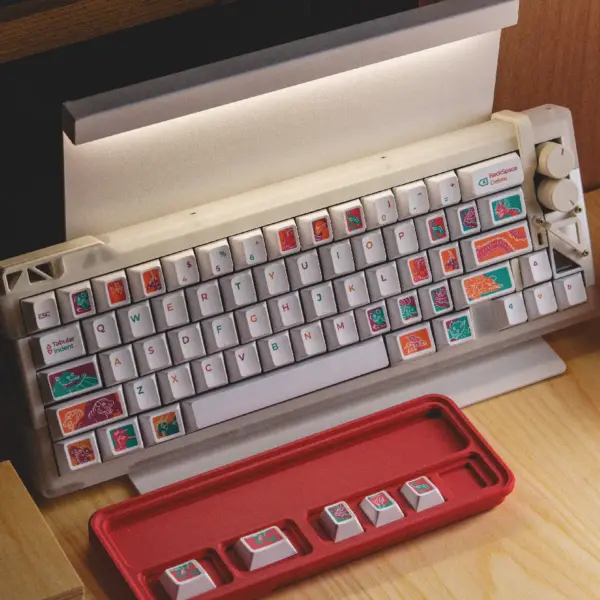 White keyboard fitted with colorful Fantasy Tunnel mythical creature keycaps beside a red tray.