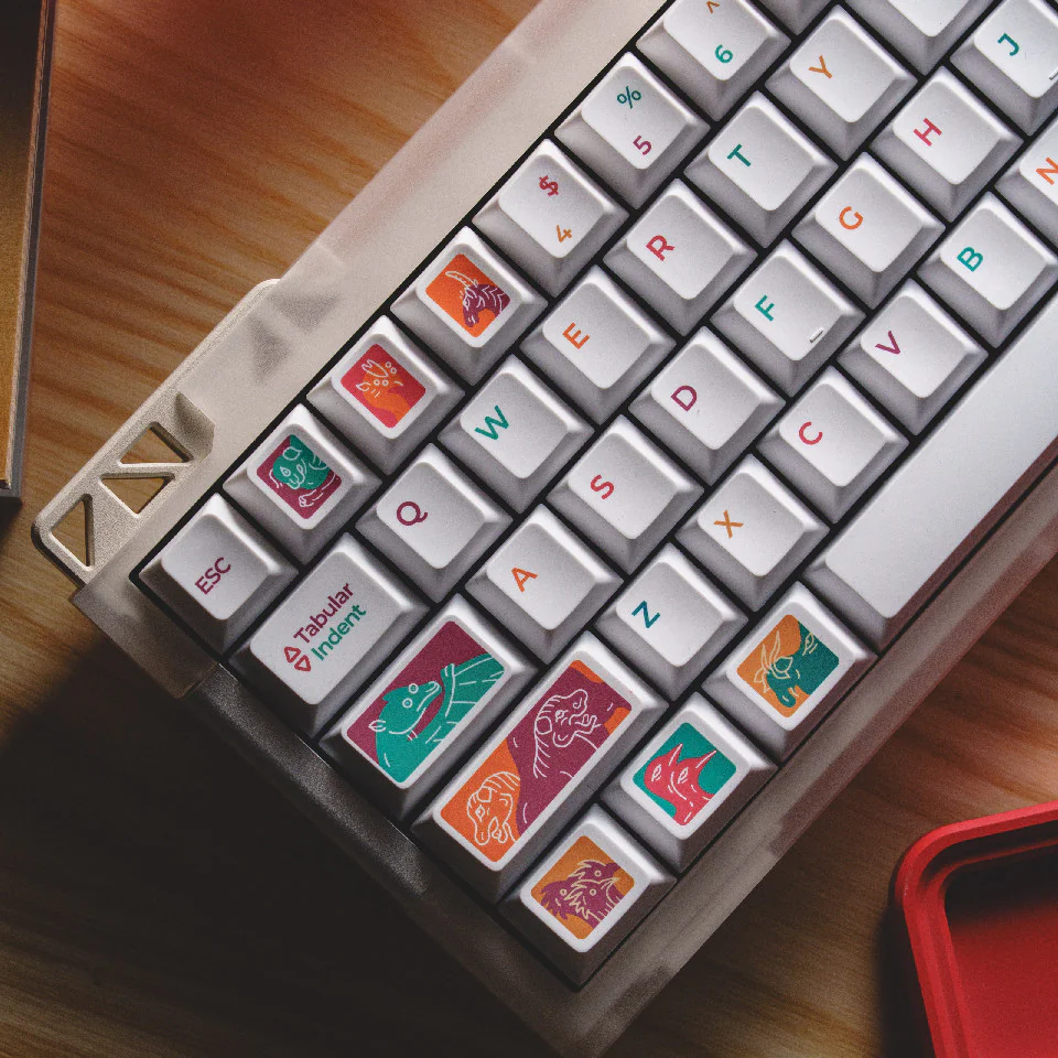 Close-up of the left side of a white keyboard with colorful creature keycaps on modifier keys.